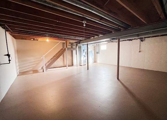 A spacious attic room with wooden beams and a staircase.