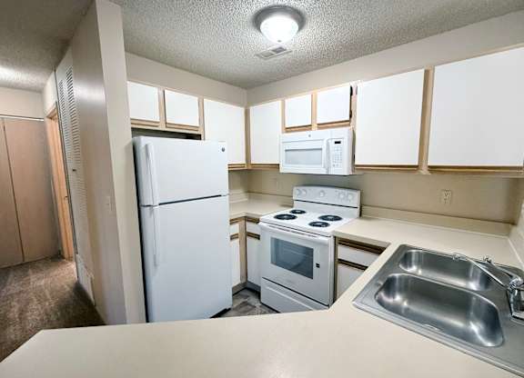 A kitchen with a white refrigerator, microwave, oven, and sink.