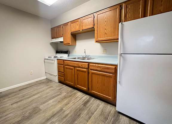 A kitchen with a white refrigerator, wooden cabinets, and a white stove top oven.