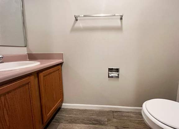 A bathroom with a toilet, sink, and wooden cabinet.