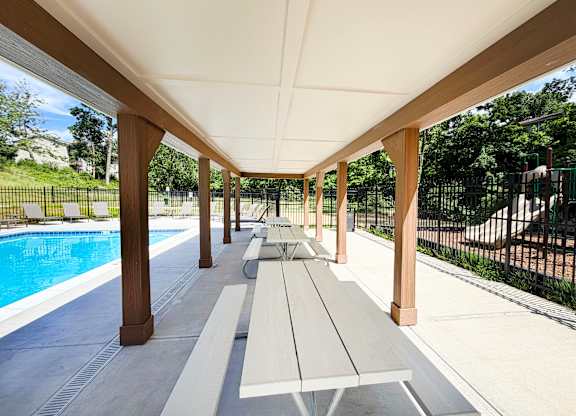 A long covered walkway with benches and a pool in the background.