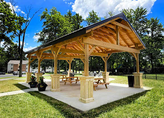 A wooden pavilion with picnic tables is surrounded by green grass.