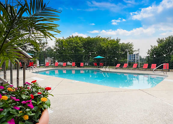 A pool surrounded by red chairs and a green umbrella.