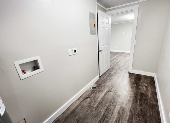 an empty room with white walls and a white door and a hallway with wood floors at Wentworth Estates Apartments, Florence, KY