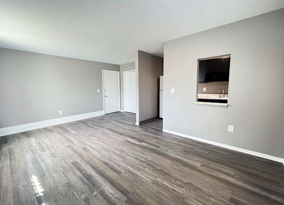 A room with wooden flooring and a small kitchenette in the corner.