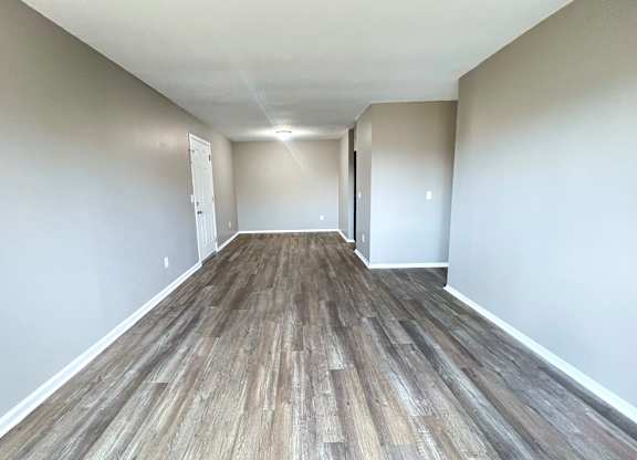 A long, empty room with wooden flooring and white walls.