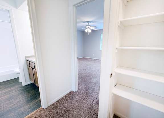 A white shelving unit is in a room with a carpeted floor and a ceiling fan.