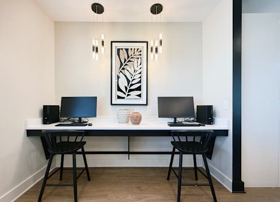 A black and white photo is on the wall above a desk with two computers and two speakers.