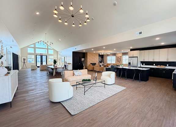 A spacious living room with a large chandelier and a kitchen area in the background.