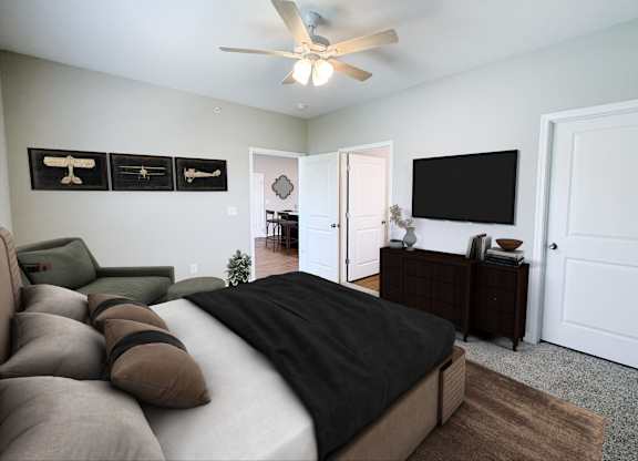 A bedroom with a bed, couch, and a television mounted on the wall.