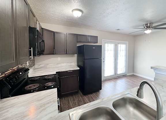 A kitchen with a black refrigerator and stove top oven.