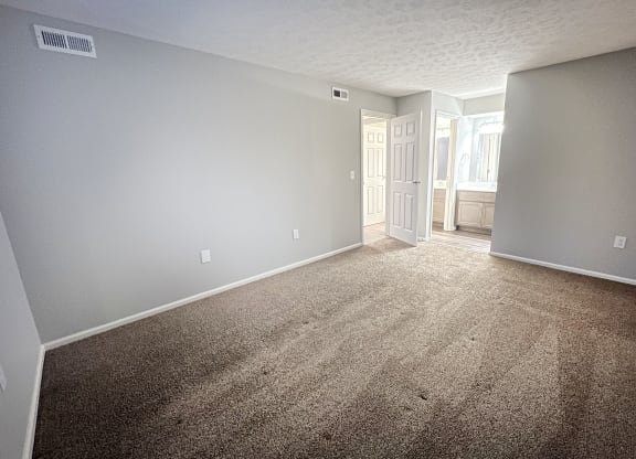 an empty living room with carpet and a door to a bathroom  at Deercross Apartments, Cincinnati