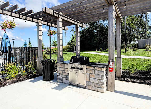 A wooden pergola with a grill and trash cans underneath it.