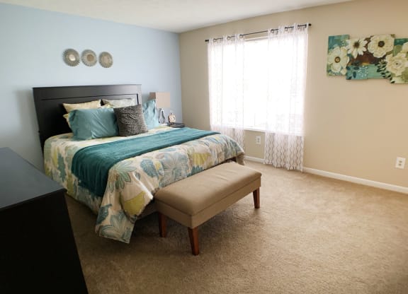 a bedroom with a bed and a chair and a window at The Vinings Apartments, Cincinnati