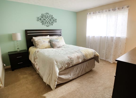 a bedroom with a bed and a dresser and a window at The Vinings Apartments, Cincinnati, OH, 45245
