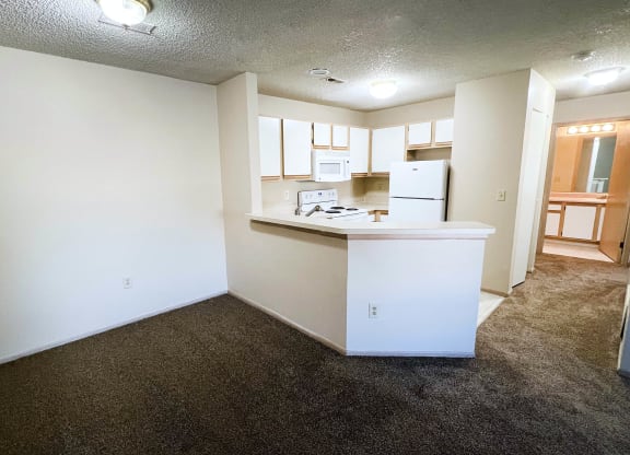 an empty living room and kitchen with white walls and a brown carpet at Eagle Crest Apartments, Galloway, Ohio
