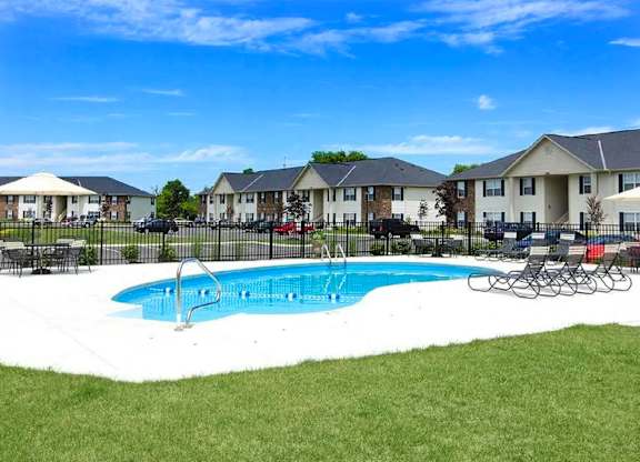 A swimming pool in a grassy area with chairs and umbrellas.