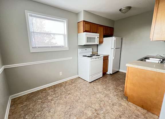 an empty kitchen with white appliances and a window