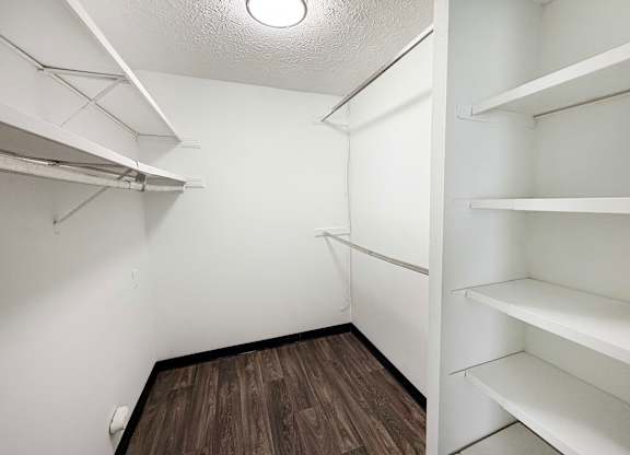 A walk-in closet with white shelves and a wooden floor.
