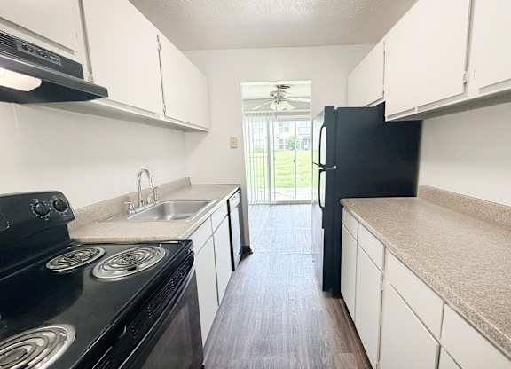 A black stove top oven sits in a kitchen with white cabinets and a black refrigerator.