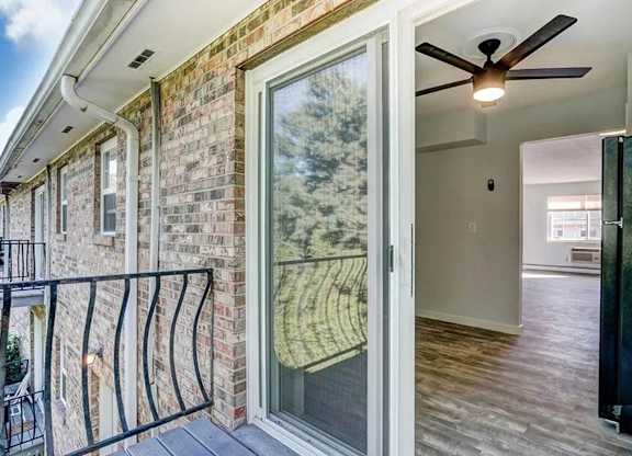 A balcony with a black railing and a glass door leading to a room with a ceiling fan.
