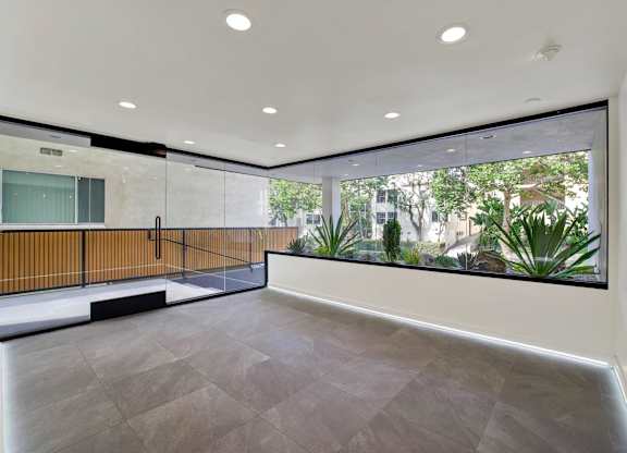 A spacious room with a grey floor and a large window overlooking a garden.