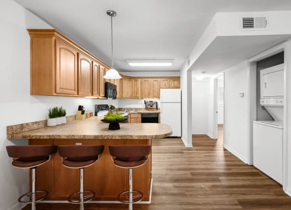 A kitchen with barstool seating, upgraded lighting, oak cabinets, and white appliances with a stackable washer and dryer included.