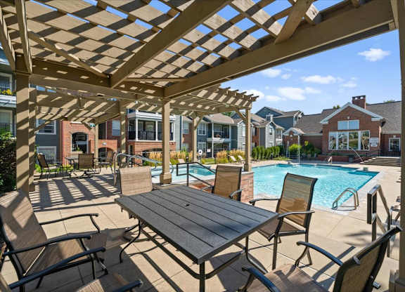 A wooden pergola over a table with chairs and a pool in the background at Somerset Oaks Apartment Homes, Olathe, 66062