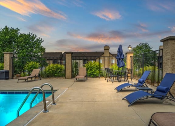 a swimming pool with blue chairs and umbrellas    and a fence at Deerfield Apartments, Kansas