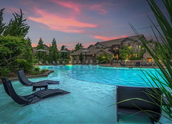 A pool with loungers and a house in the background during sunset.