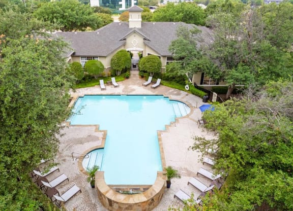 a swimming pool with lounge chairs and trees in the background