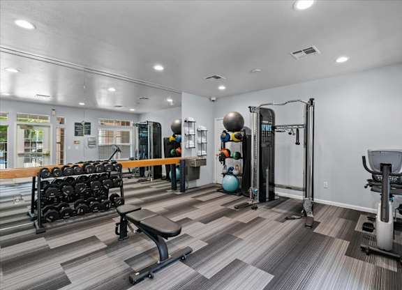 A gym with a variety of equipment including a squat rack, dumbbells, and a bench.at Crowne Chase Apartment Homes, Overland Park, KS