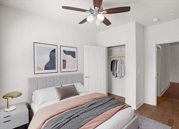 A bedroom with a ceiling fan, clothes closet, and hardwood floors.
