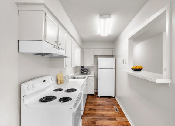 A kitchen equipped with a dishwasher, range with stove and oven, refrigerator, and hardwood floors.