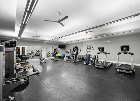 Spacious fitness center at West 39th Street Apartments featuring treadmills, ellipticals, recumbent bikes, free weights, and large wall mirrors at West 39th Street Apartments, Kansas City, MO