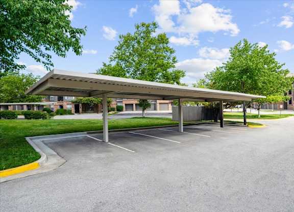 A parking lot with a covered parking area and trees in the background.