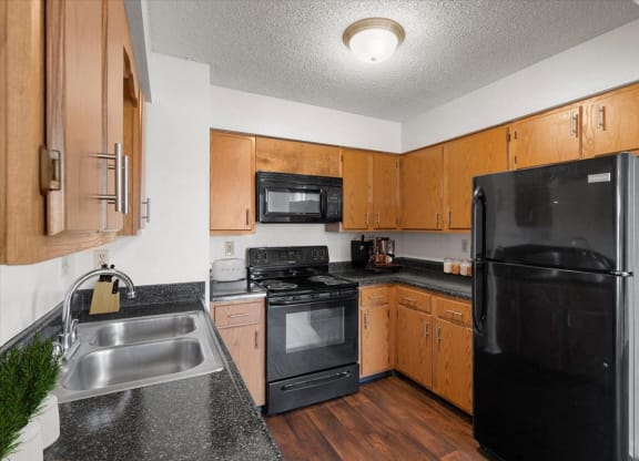 a kitchen with black appliances and wooden cabinets at Deerfield Apartments, Olathe, Kansas