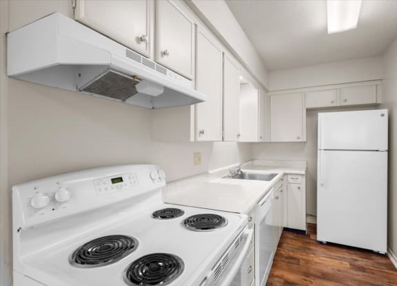 A kitchen with hardwood floors and white appliances including a dishwasher.