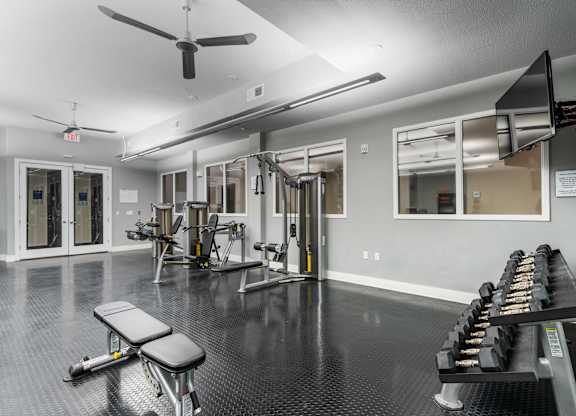 Free weights, strength machines, and mounted TV in fitness center at West 39th Street Apartments, Missouri, 64111