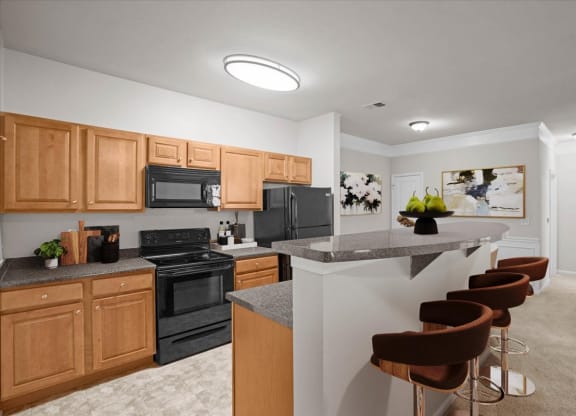 An open kitchen with barstool seating, oak cabinetry, black appliances, and lots of counter space.