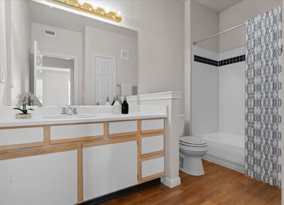 A bathroom with a tub shower combo, a large vanity mirror, plenty of counter space, and storage cabinets and drawers under the sink.