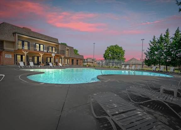 A large outdoor swimming pool surrounded by lounge chairs and a building with a balcony.