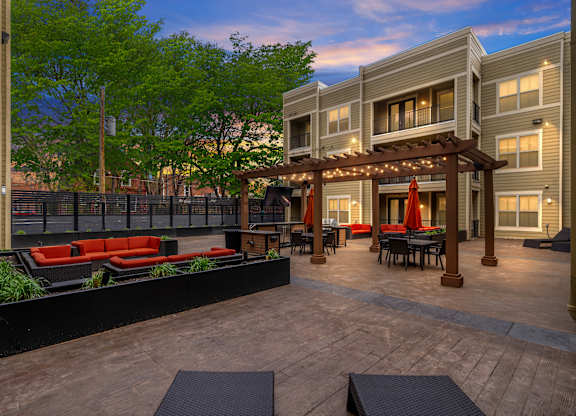 Courtyard at West 39th Street Apartments featuring seating areas, greenery, and pergola with lights at dusk at West 39th Street Apartments, Kansas City