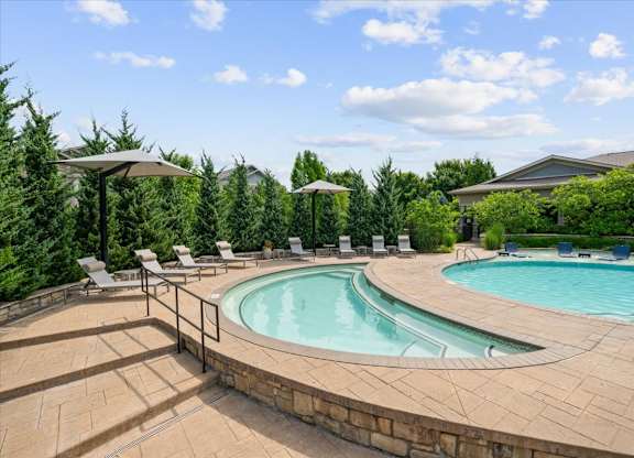 A large outdoor swimming pool surrounded by a stone wall and lounge chairs.