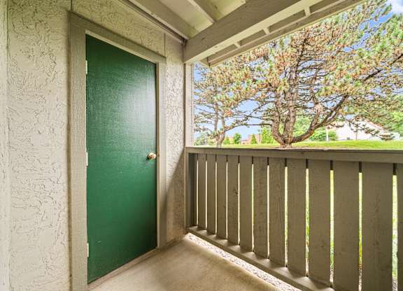A green door is on the left of a balcony with a view of trees.