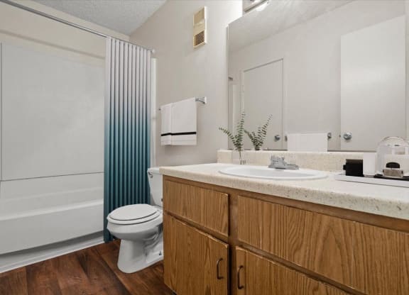 A bathroom with wooden storage cabinets, a large vanity mirror, lots of counter space, a toilet, and a tub shower combo.