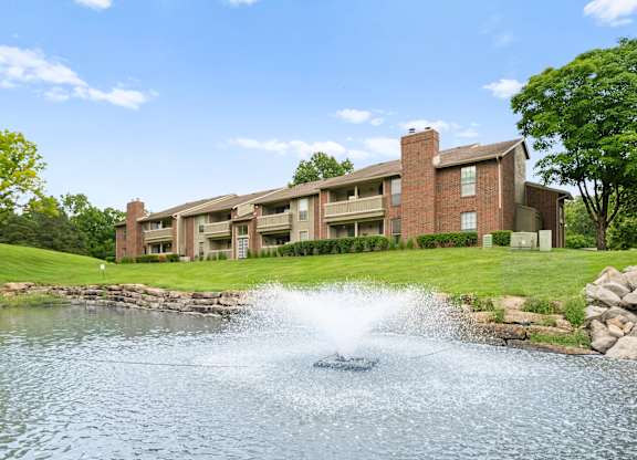 A fountain in the middle of a pond in front of a building.