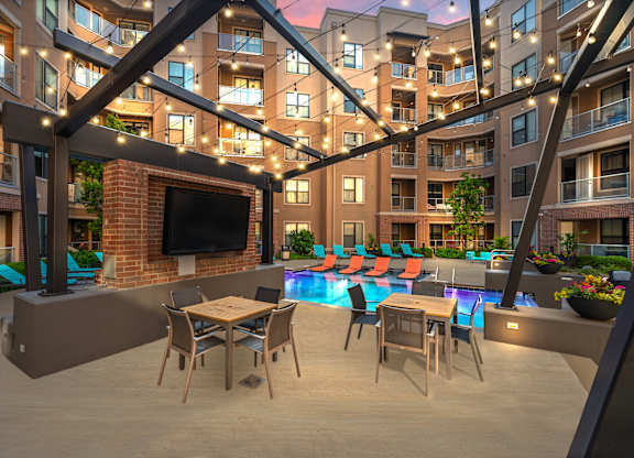 A modern outdoor patio area with a television, seating, and a pool.