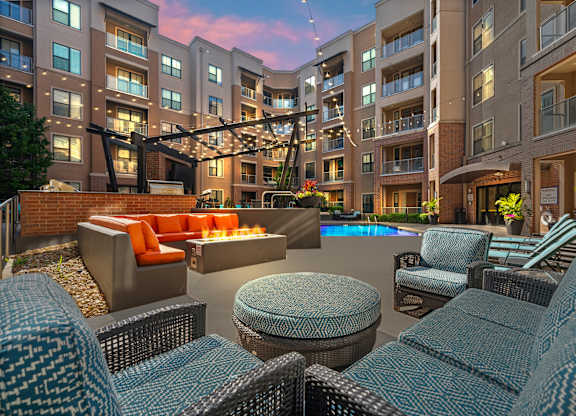 A large outdoor seating area with wicker chairs and tables is surrounded by apartment buildings.