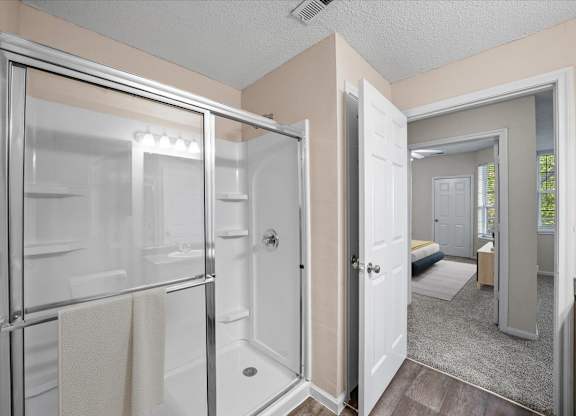 A bathroom with a glass shower door and a white door.at The Claremont Apartment Homes, Overland Park